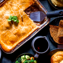 potato and meat multi-portion pie surrounded by pasties, cakes and fresh veg