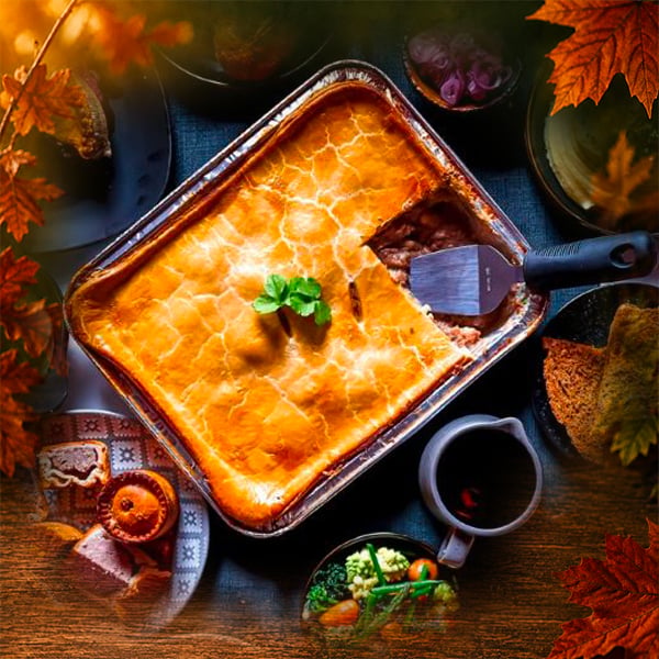 Golden multiportion pie in a foil tray with a slice served, alongside gravy and vegetables, surrounded by autumn leaves