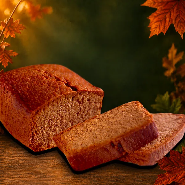 Sticky parkin cake loaf cut open to show its soft golden crumb, styled with pine cones and autumn pumpkins
