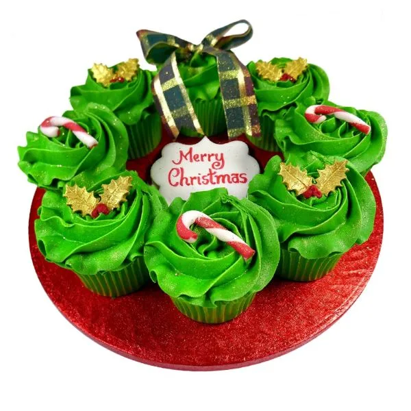 Christmas cupcake wreath with green swirled cupcakes, gold holly leaves, candy canes and a tartan bow on a red board